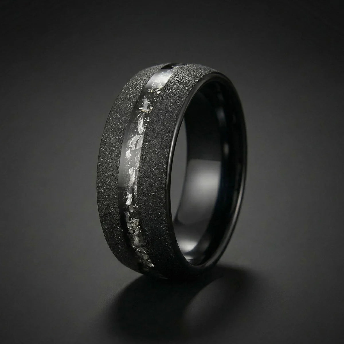 Black Meteorite Tungsten Ring close up resting on rustic concrete surface with accent stone