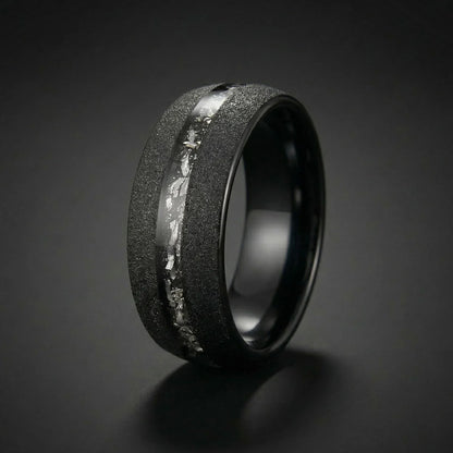 Black Meteorite Tungsten Ring close up resting on rustic concrete surface with accent stone