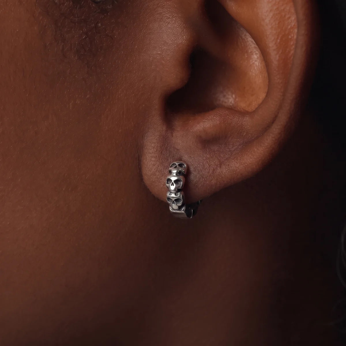 Multi Skull Head Huggie Earrings Silver Worn by Model Close Up Dark Lighting